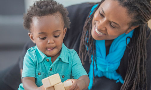 Mom smiles at son as he plays with blocks.